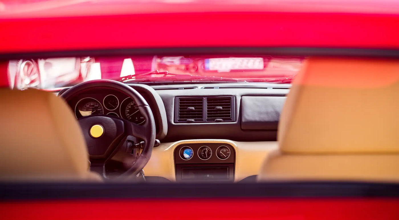 Car dashboard viewed through a windshield with tan interior and black steering wheel.