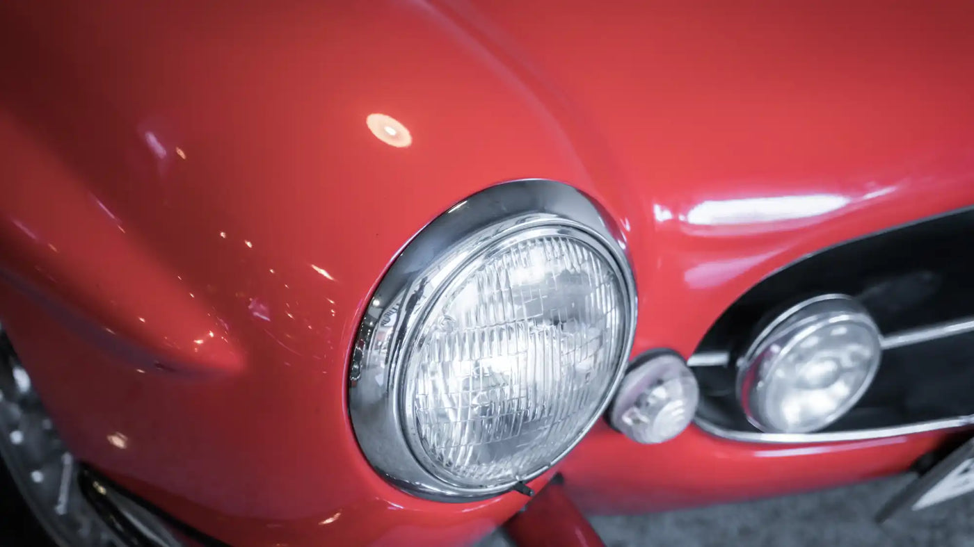 Round chrome headlight mounted on glossy red automotive bodywork.